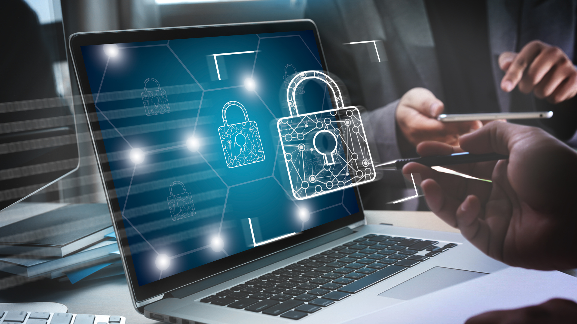 Laptop displaying digital padlock icons representing data security, with a person holding a phone.